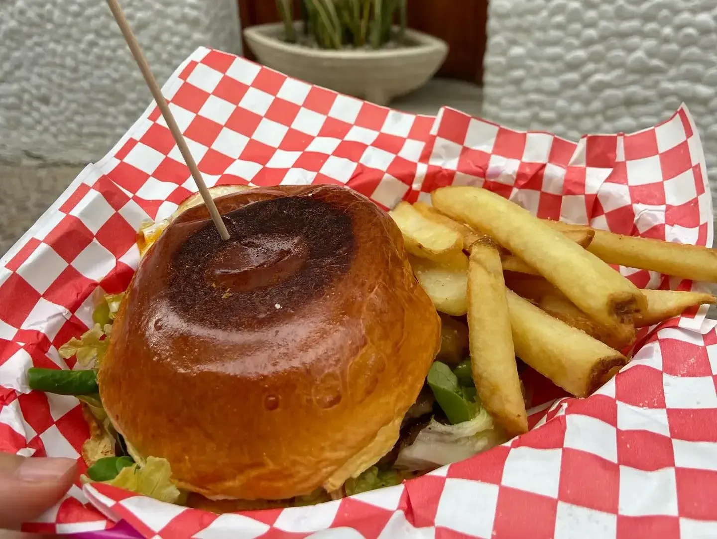 Hamburguesa a la parrilla en una bandeja a cuadros con papas fritas y un palillo de dientes.