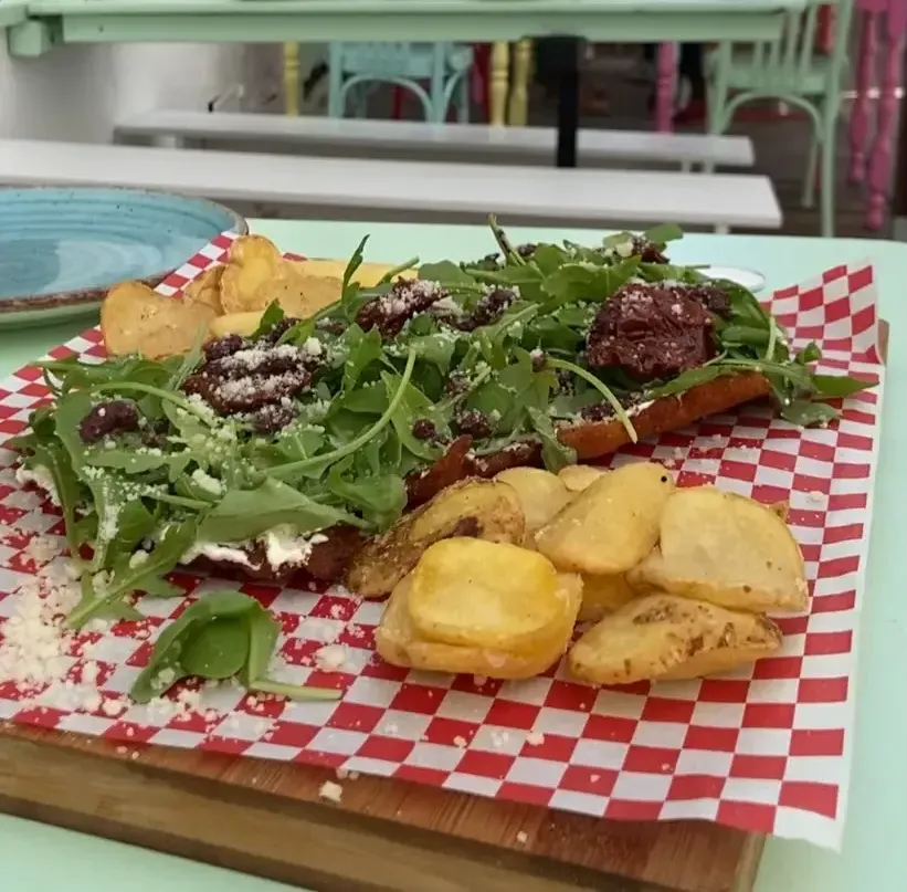 Ensalada de rúcula con carne a la parrilla y patatas gajo doradas en plato de papel a cuadros rojos y blancos.