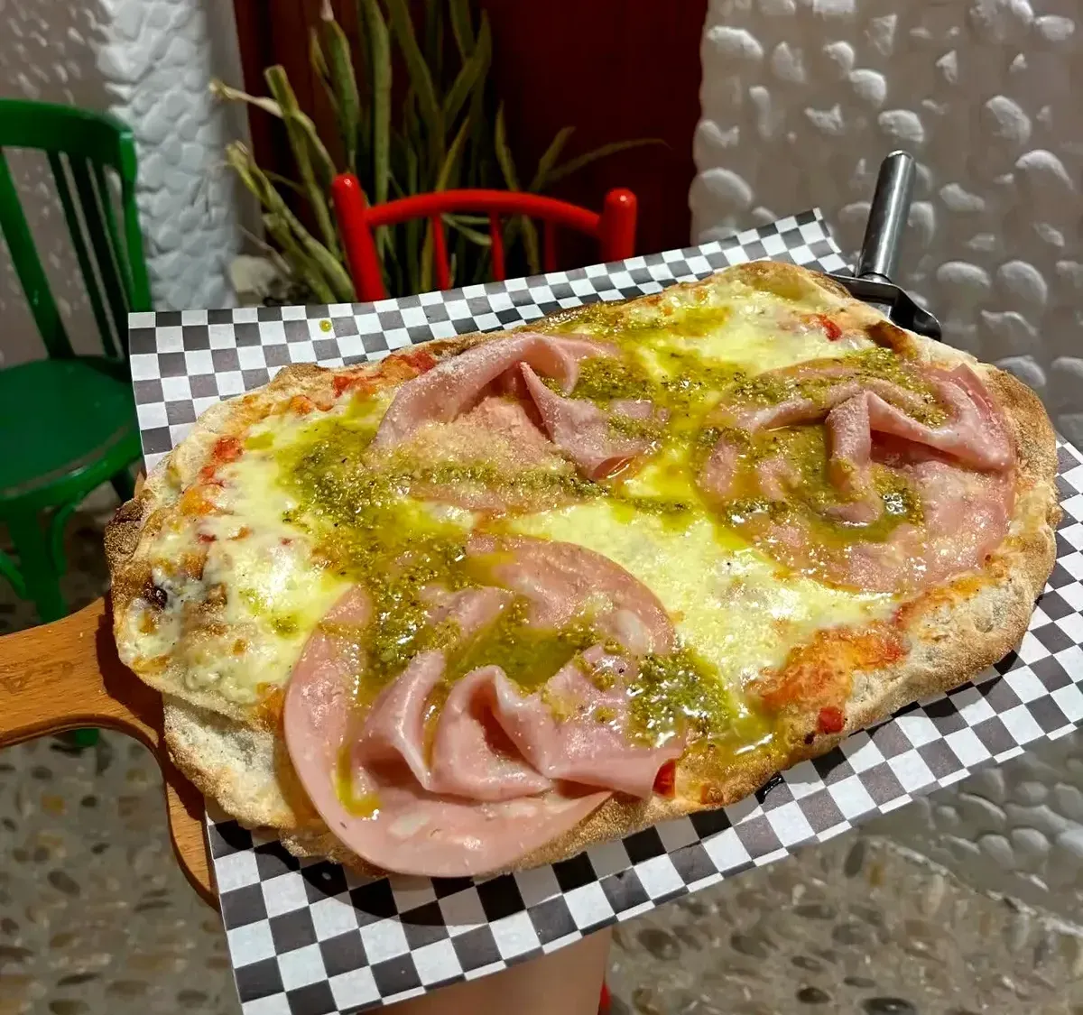 Pizza ovalada con queso fundido y lonchas de jamón dobladas sobre una bandeja a cuadros blancos y negros.