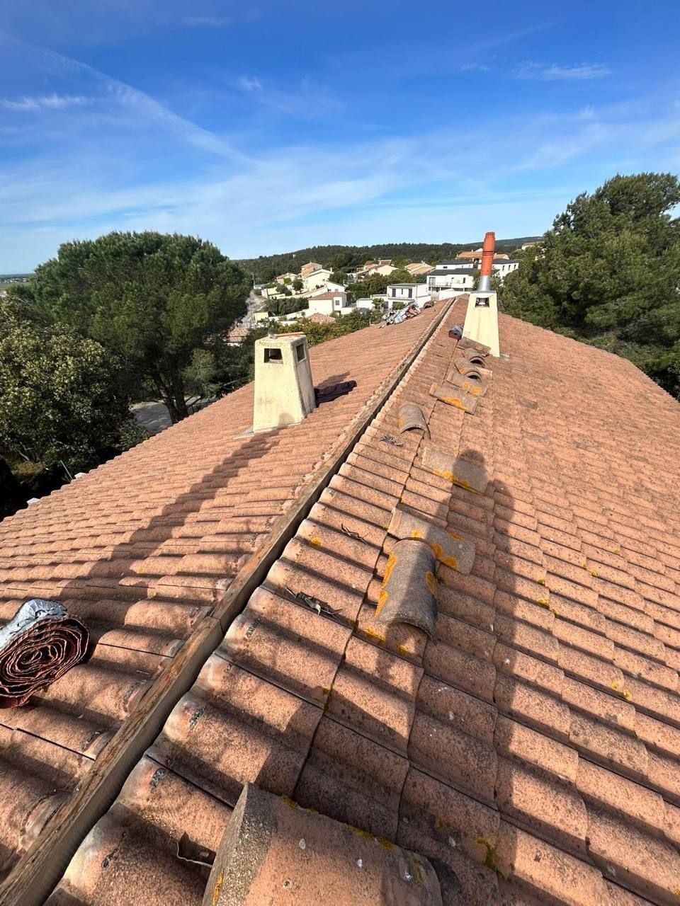 Vue d'un toit de tuiles en terre cuite avec plusieurs cheminées, se détachant sur un ciel bleu .