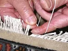 Eine Person näht einen Teppich mit Nadel und Faden.