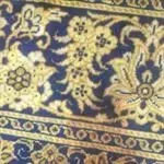 Eine Nahaufnahme eines blau-goldenen Blumenmusters auf einem Teppich.