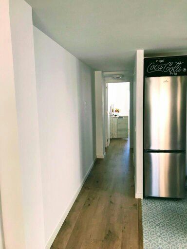 Un pasillo con un refrigerador de acero inoxidable y un cartel de Coca Cola en la pared.