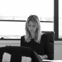 Femme en haut sombre, regardant vers le bas, assise à un bureau près de la fenêtre. Noir et blanc.
