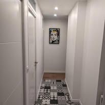 Couloir étroit aux murs blancs et au sol à motifs colorés. Un portrait est accroché au fond.