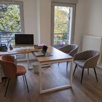Espace de travail avec meuble de bureau, ordinateur portable, chaises et fenêtres laissant entrer la lumière naturelle.