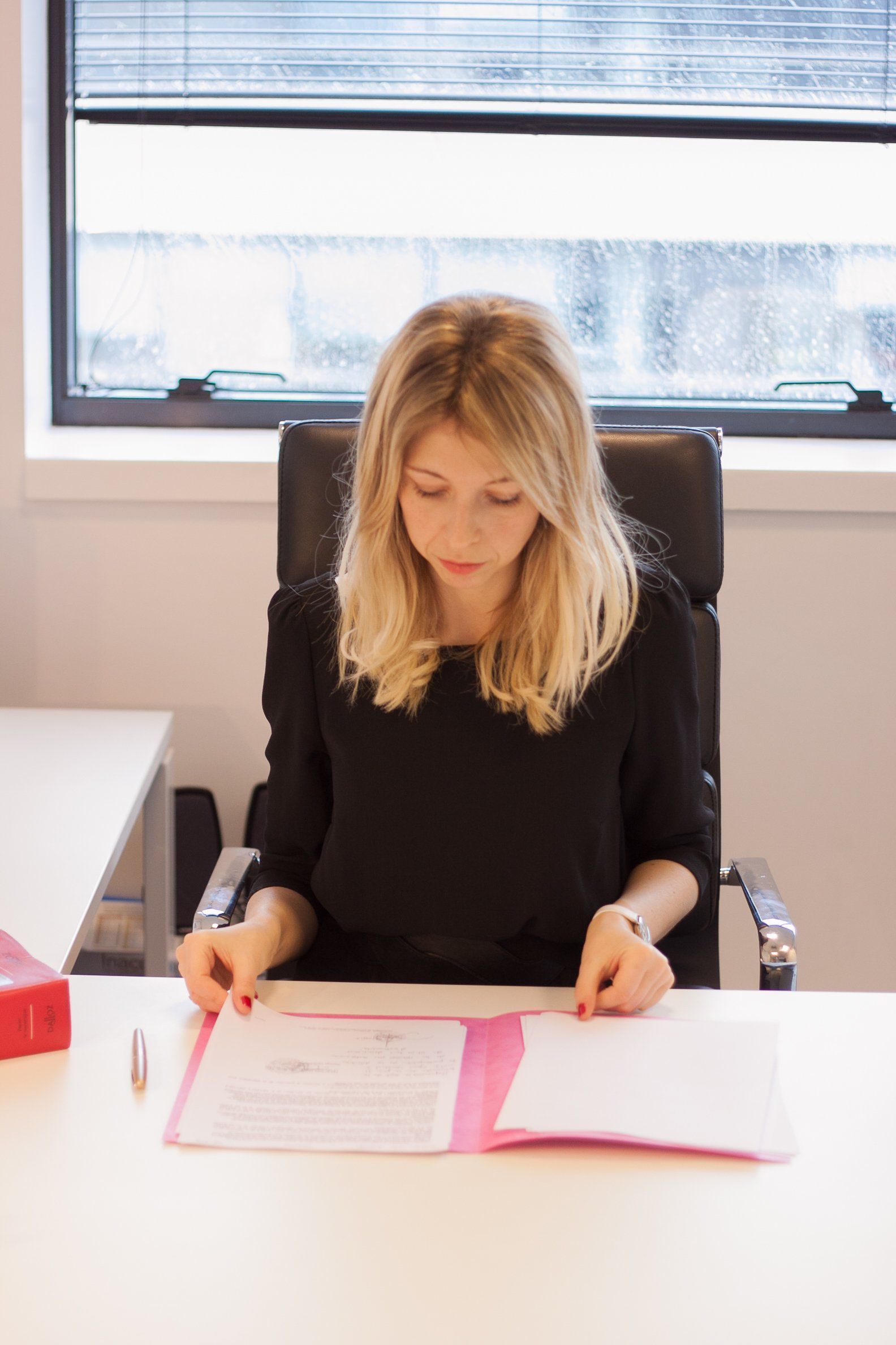 Une femme en haut noir examine des documents à un bureau.