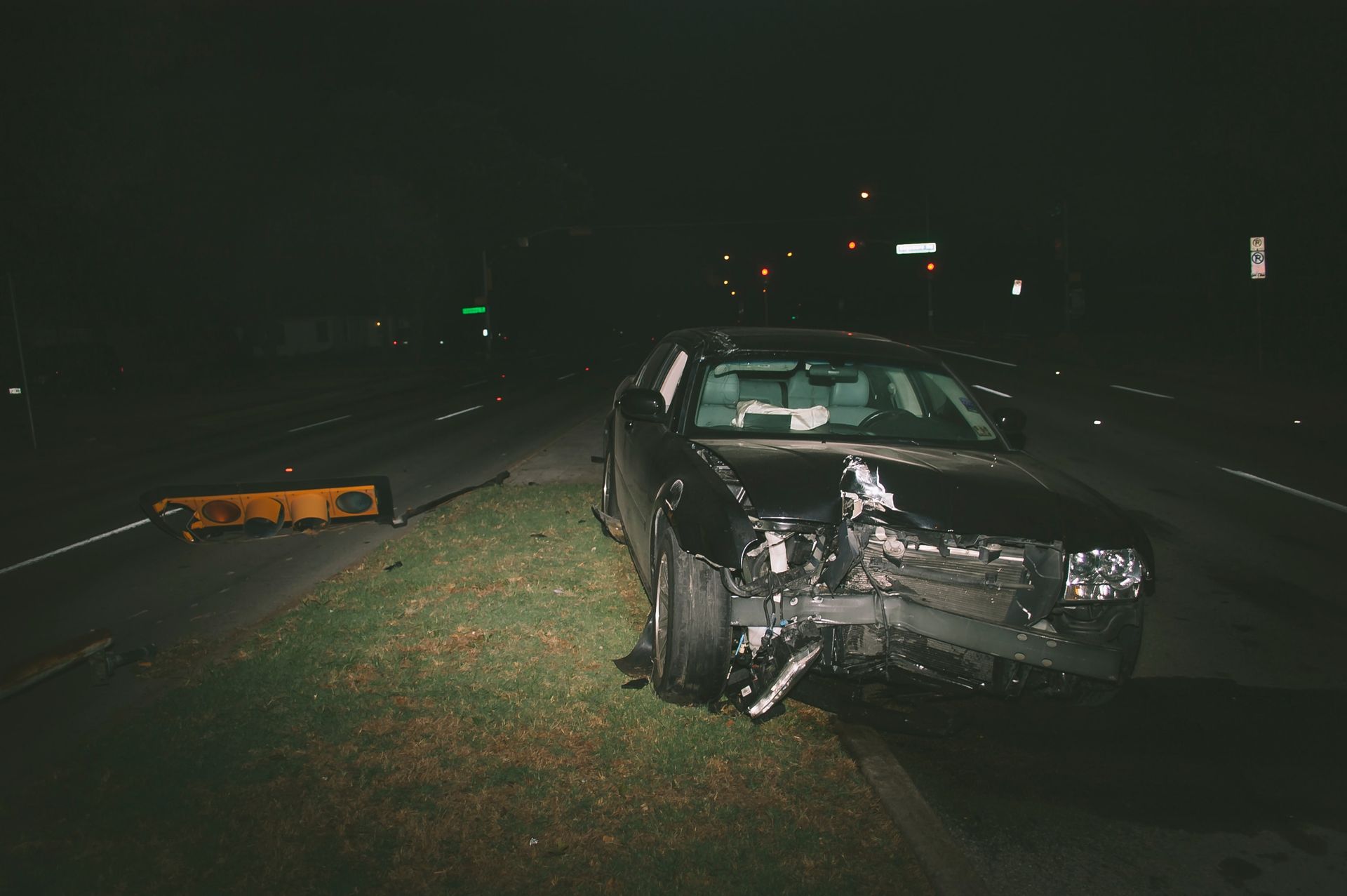 Voiture noire endommagée lors d'un accident nocturne en bord de route, avec des dégâts visibles à l'avant.