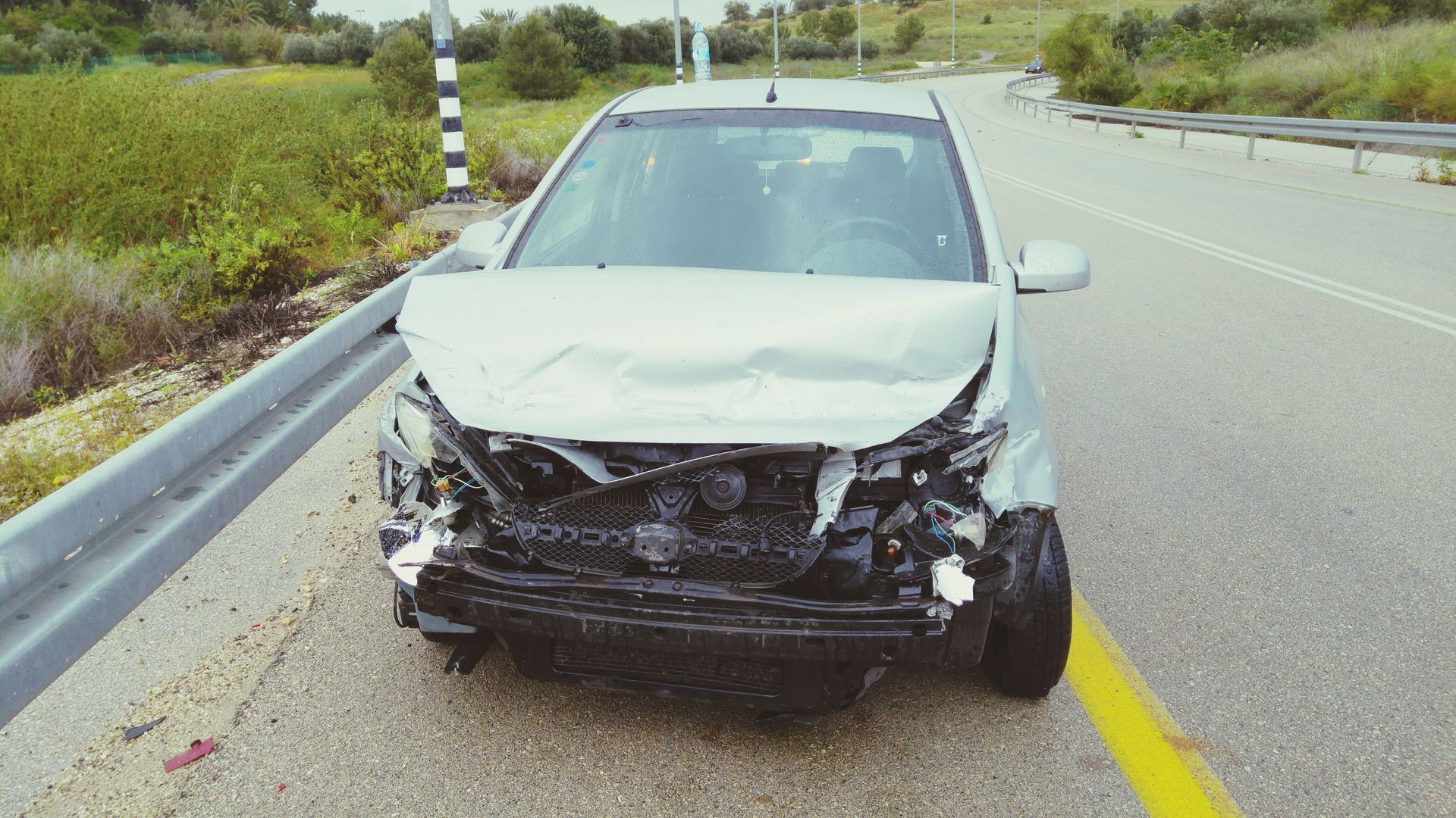 Voiture argentée endommagée sur le bord de la route après une collision ; avant froissé.