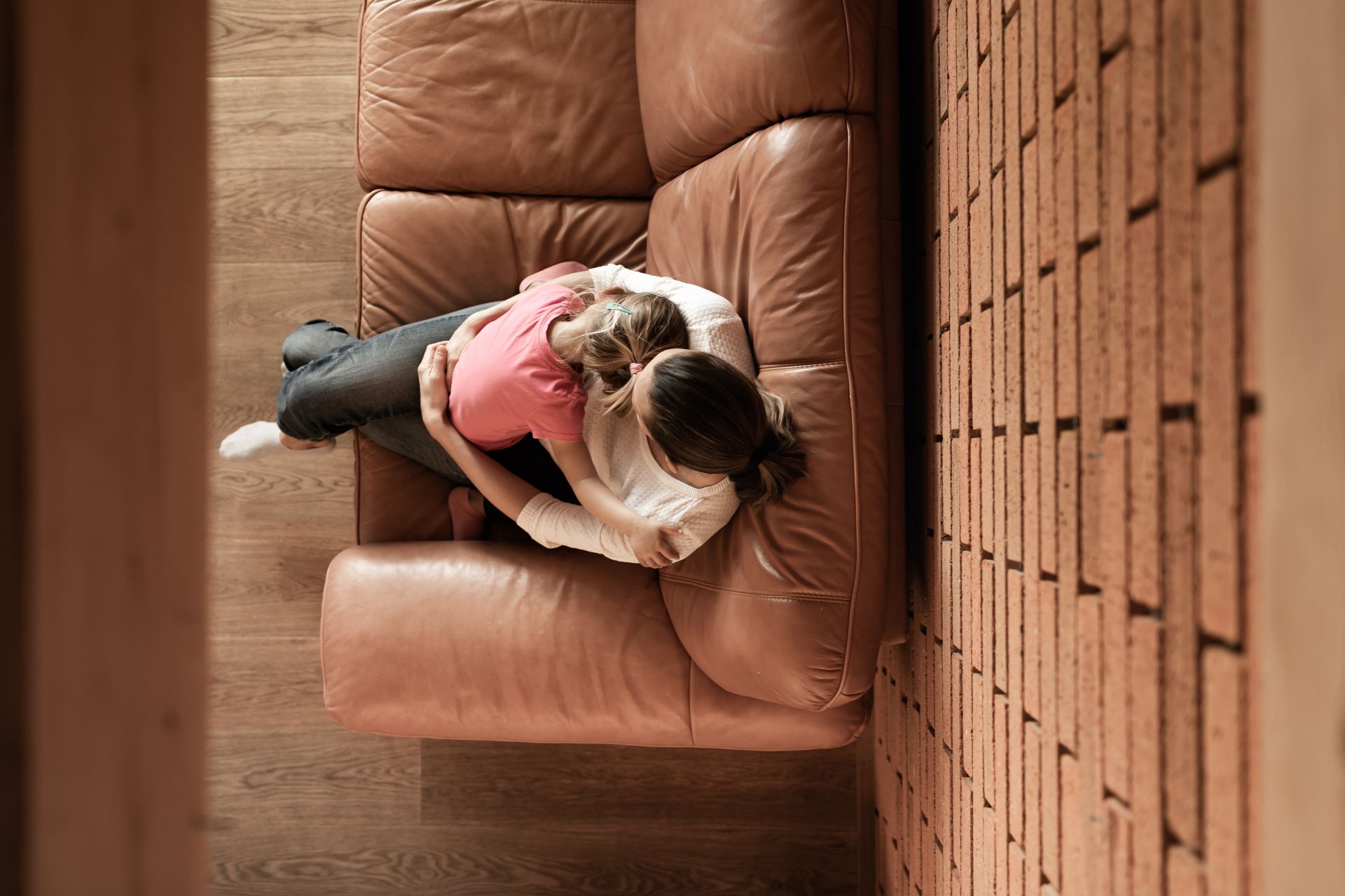 Deux personnes s'enlacent sur un canapé en cuir marron dans une pièce avec un mur de briques.