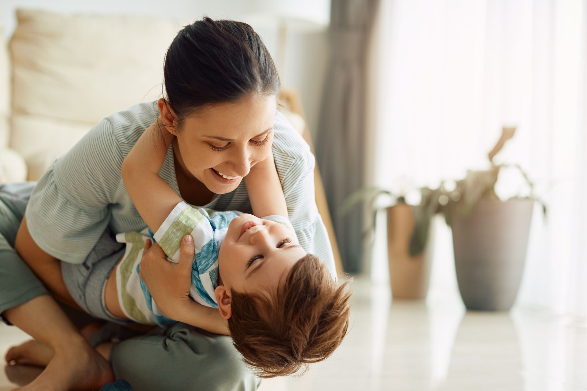 Une femme et un enfant sourient et jouent par terre.