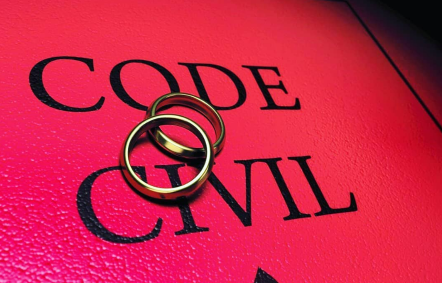Deux alliances en or sur un livre rouge portant l'inscription CODE CIVIL.