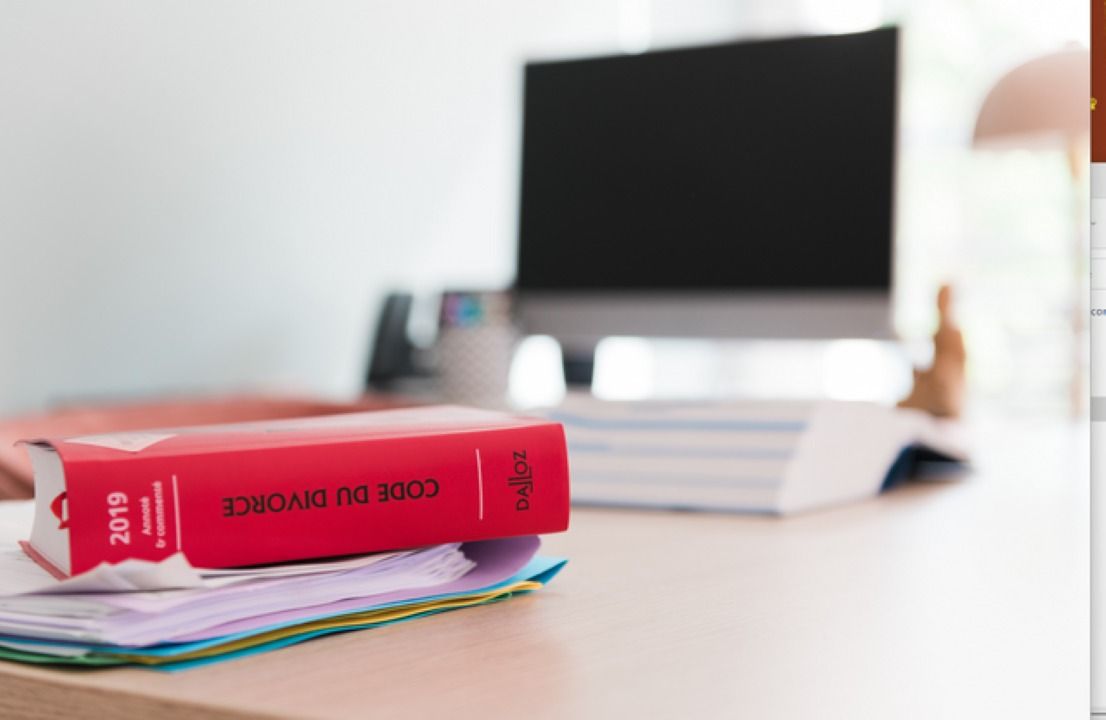 Le livre de lois rouge Code de divorce 2019 est posé sur un bureau, avec un ordinateur en arrière-plan.