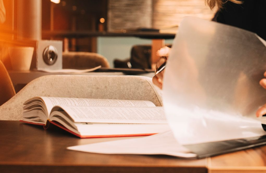 Une personne étudie, feuilletant un livre ouvert, assise à une table avec une tasse de café.