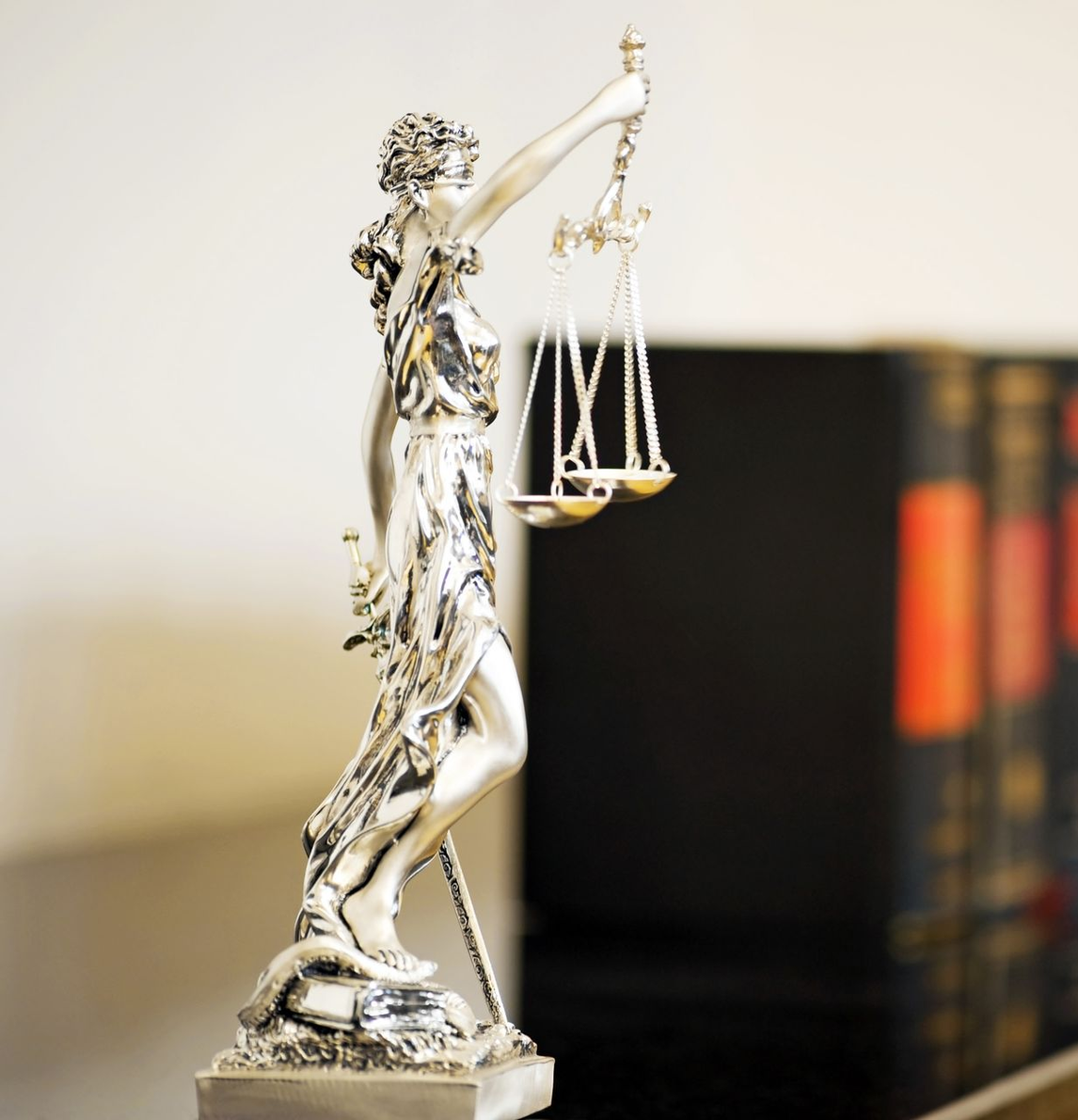 Statue de la balance de la Justice, en argent, avec des livres de lois en arrière-plan.