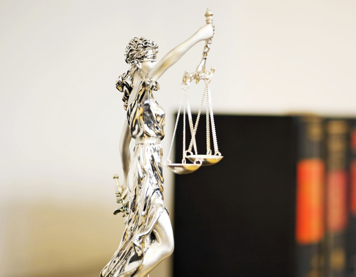 Statue de la Justice tenant une balance, livres en arrière-plan. Sculpture en argent, fond blanc.