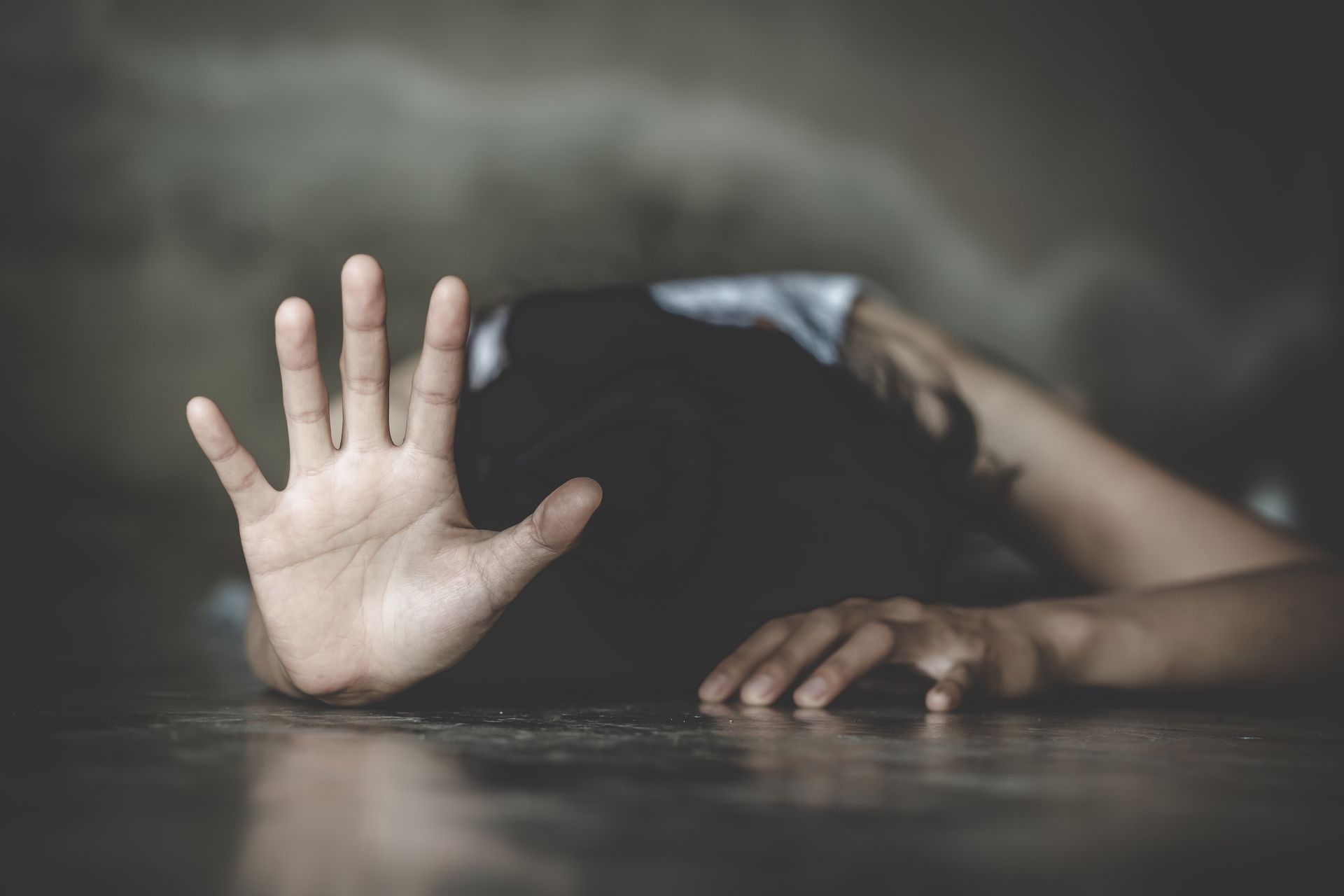 Une personne allongée au sol, la main levée en signe d'arrêt, semble en détresse.