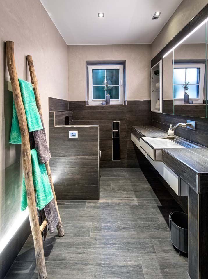 Badezimmer mit Holzleiter, an der Handtücher hängen, dunklen Holzelementen, Waschbecken, Toilette und Fenster.