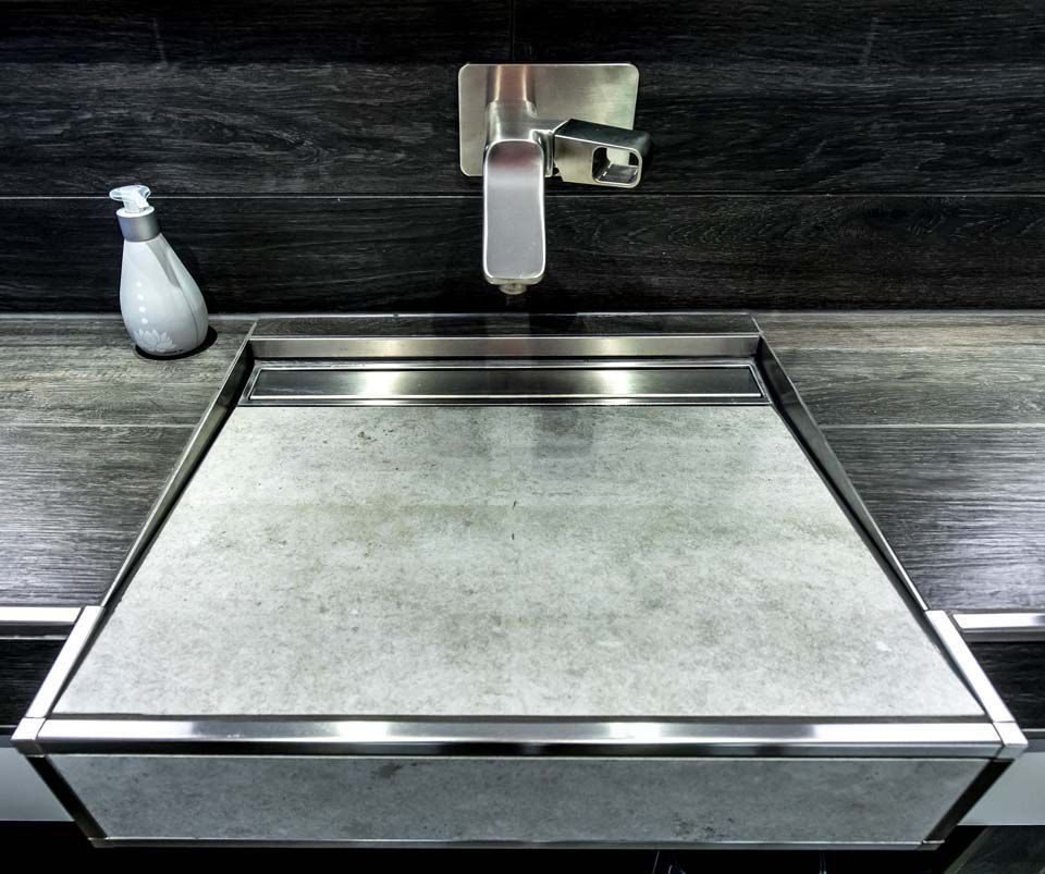 Eingebautes Waschbecken mit Granitbecken und Edelstahlverkleidung. Armatur und Seifenspender sind sichtbar. Dunkler Fliesenhintergrund.