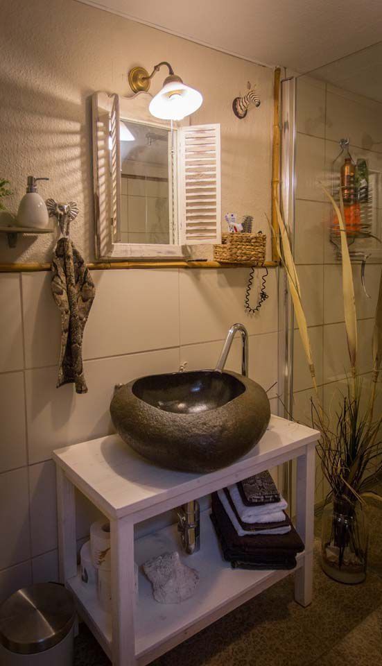 Badezimmer mit Steinwaschbecken auf weißem Schrank, Spiegel und Dekorationselementen.