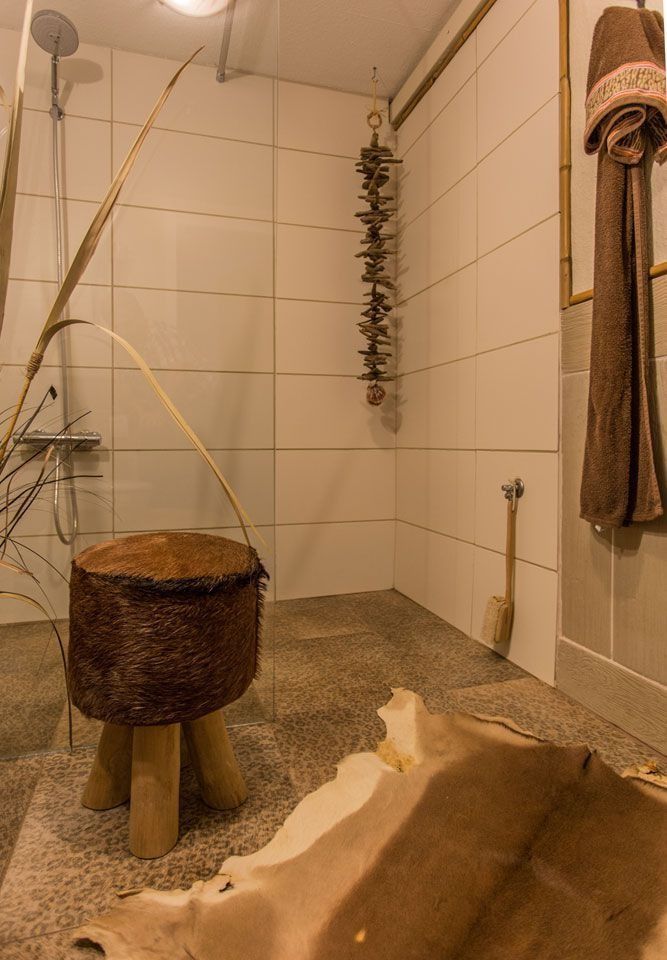 Rustikales Badezimmer: Holzschemel, Tierfellteppich, geflieste Wände, Duschkopf und hängende Dekoration.