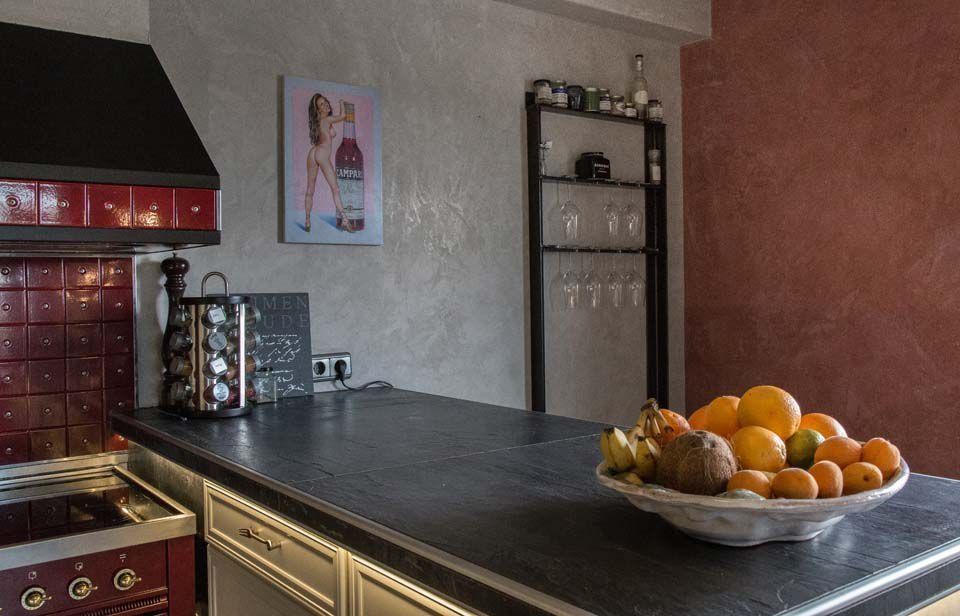 Küche mit schwarzer Arbeitsplatte, rotem Herd, Obstschale und Wandbild. Graue und rote Wände, Metallregale.