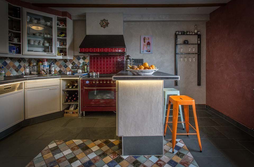 Küche mit rotem Herd, orangefarbenem Hocker und farbenfrohem Fliesenspiegel.