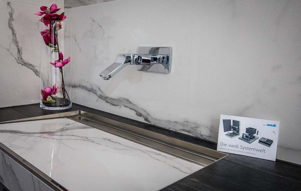 Modernes Badezimmerwaschbecken mit Marmorarbeitsplatte und wandmontierter Armatur. Vase mit rosa Blumen.