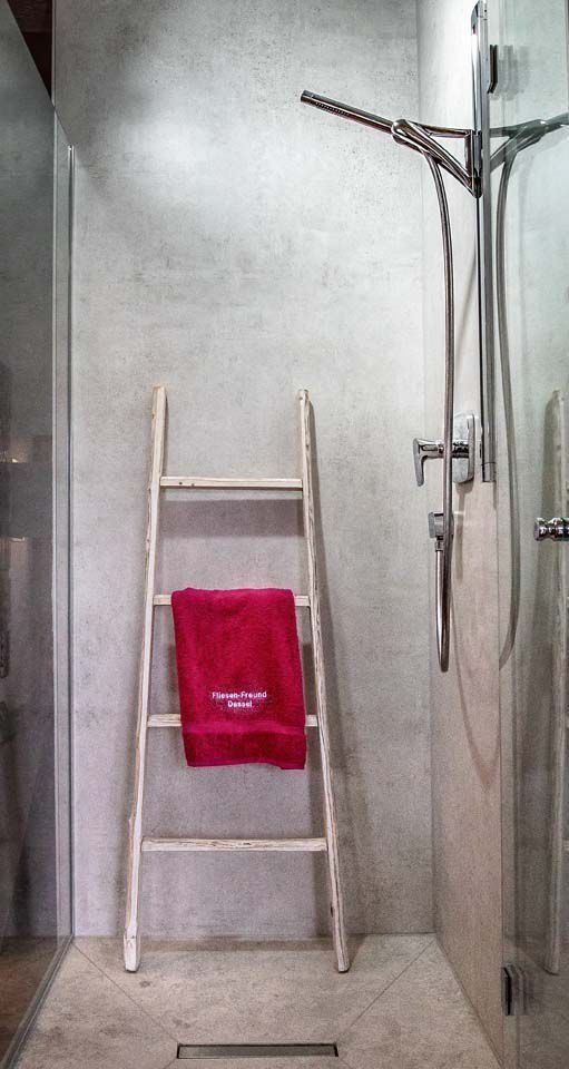 Ein kleines Badezimmer mit einem roten Handtuch, das über eine Holzleiter gehängt ist, daneben eine Dusche mit Glastüren.