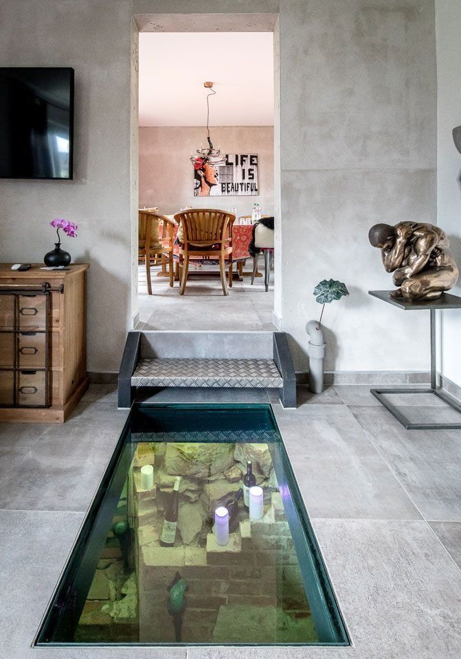 Der Innenraum verfügt über einen Glasboden, der eine tiefer gelegene Ebene mit Zugang zum Essbereich freigibt. Wände und Boden sind grau.