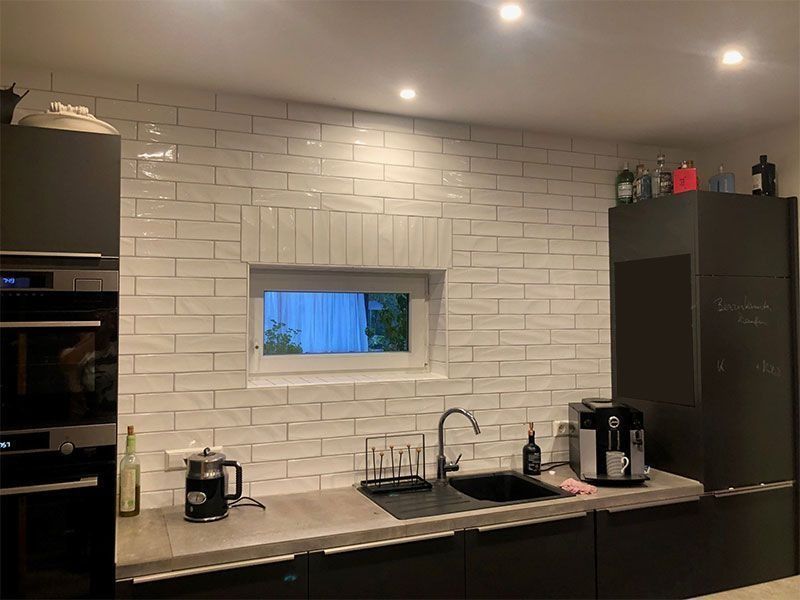 Moderne Küche mit weißer Backsteinwand als Spritzschutz, schwarzen Schränken und Edelstahlgeräten.