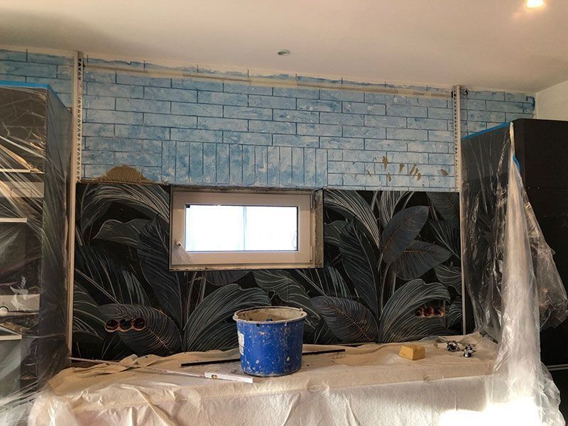 Küchenrenovierung: Blaue Backsteinwand und dunkler, floraler Fliesenspiegel, Schränke mit Plastikfolie abgedeckt.