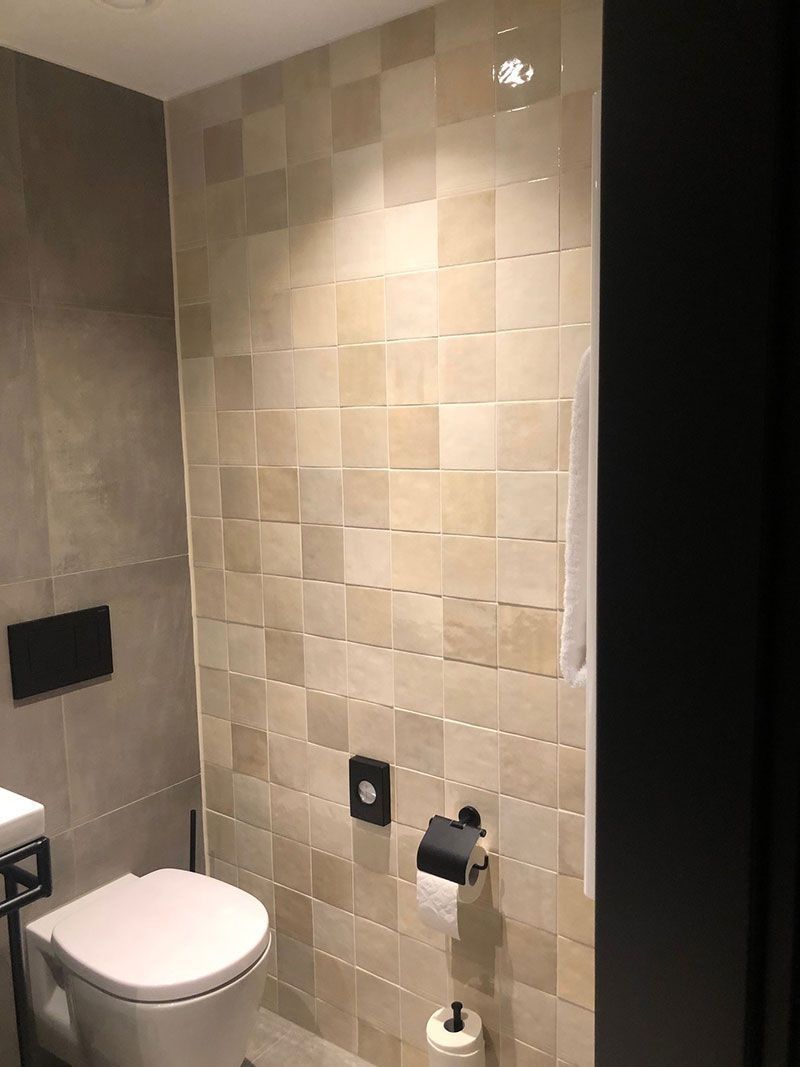 Kleines Badezimmer mit Toilette, Wandfliesen und Toilettenpapierhalter.