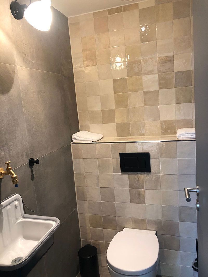 Kleines Badezimmer mit Toilette, Waschbecken und gefliesten Wänden in Beige- und Grautönen.