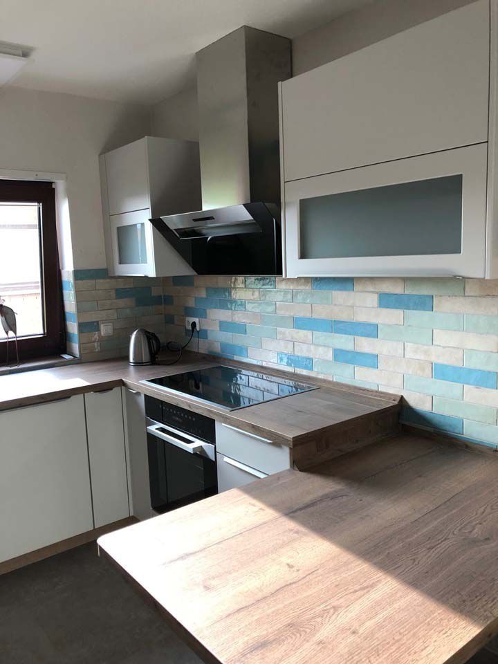 Moderne Küche mit weißen Schränken, blau-weiß gefliestem Spritzschutz, Dunstabzugshaube aus Edelstahl und Arbeitsplatten aus Holz.
