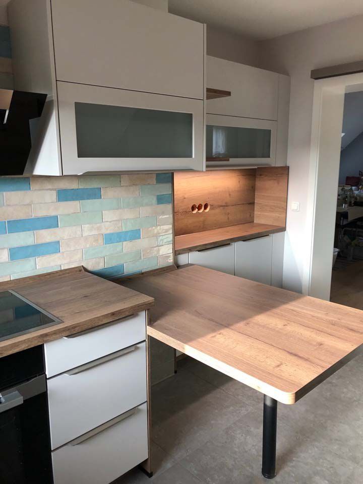 Moderne weiße Küche mit Arbeitsplatten aus Holz, blau-weiß gefliestem Spritzschutz und Klapptisch.