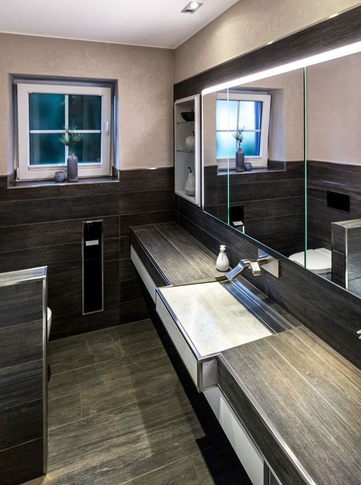 Modernes Badezimmer mit dunklen Holzmaserungsoberflächen, eingebautem Waschbecken und Spiegel, Fenster und neutralfarbigen Wänden.