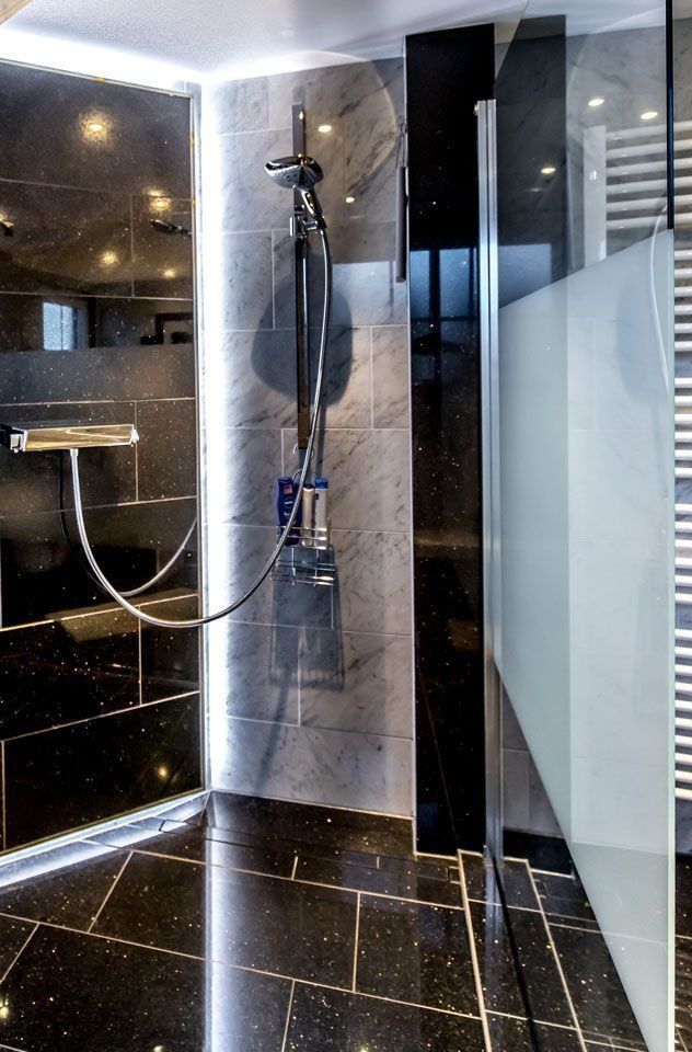 Moderne Dusche mit schwarzen Marmorfliesen und Glasabtrennung; Armaturen aus Chrom.