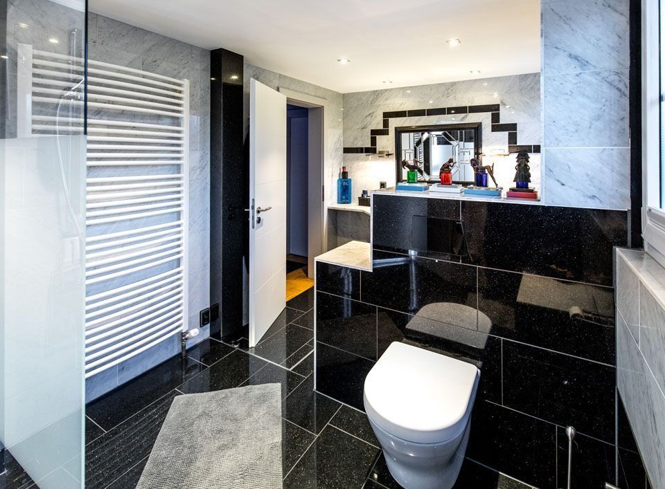 Modernes Badezimmer mit schwarz gefliesten Wänden und Boden. Weiße Toilette, Handtuchhalter und Dusche mit Milchglas.