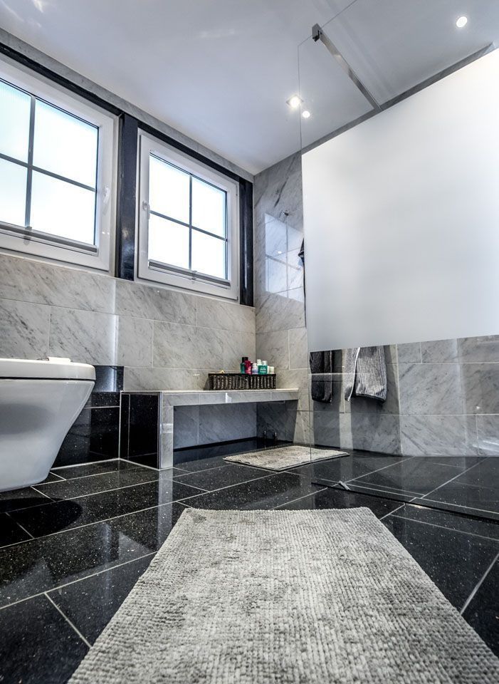 Modernes Badezimmer mit schwarzem Fliesenboden, grauen Marmorwänden und weißer Toilette.