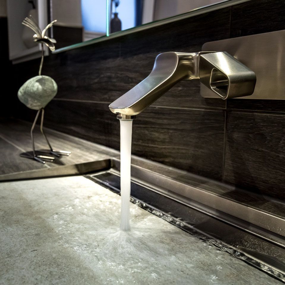 Ein Wasserhahn aus gebürstetem Metall, aus dem Wasser in ein graues Waschbecken fließt. Daneben steht ein dekorativer Vogel auf der Arbeitsplatte.