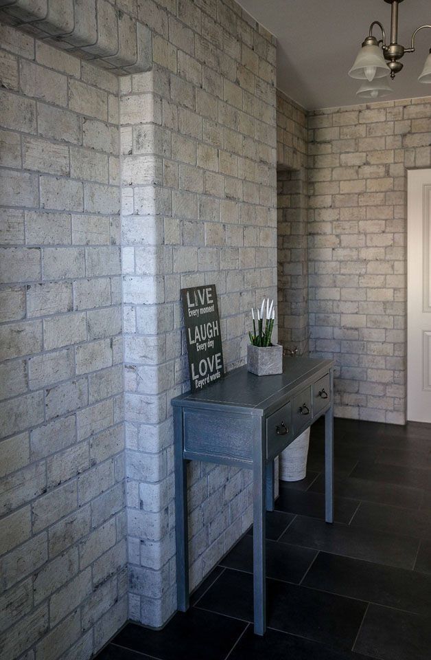 Graue Backsteinwand mit blauem Konsolentisch und dekorativem Schild. Schwarzer Fliesenboden.
