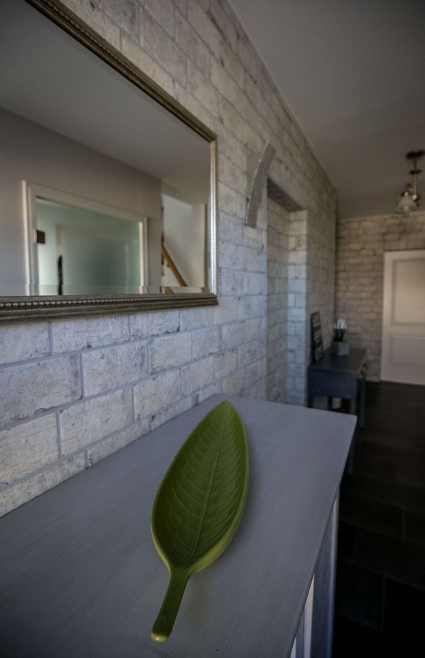 Ein modernes Interieur mit einer Wand im Backsteinmuster, einem Spiegel und einer grünen, blattförmigen Schale auf grauem Untergrund.