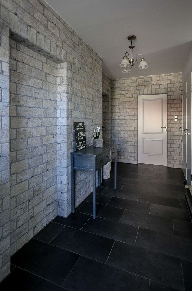 Eingangsbereich mit grauen Wänden im Backsteinstil, dunklem Fliesenboden, grauem Konsolentisch und weißer Tür.