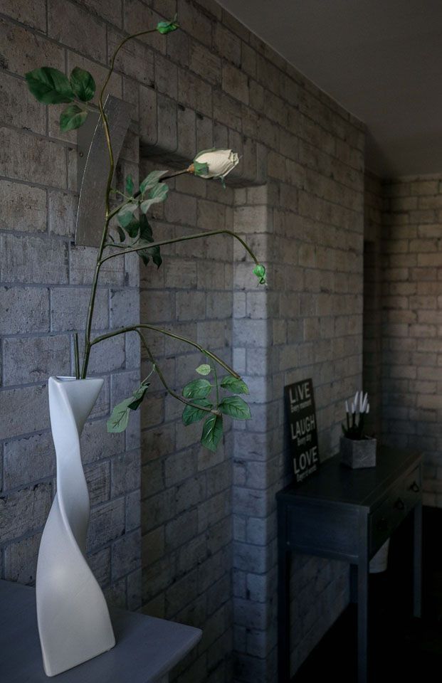 Weiße Vase mit Pflanze vor einer Backsteinwand, Beistelltisch mit Dekoration.