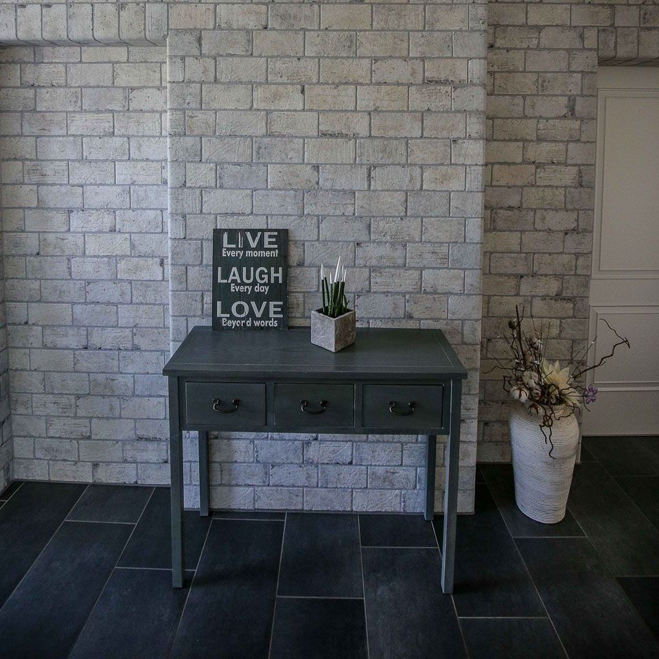 Graue Backsteinwand mit einem dunkelgrauen Konsolentisch, eingerahmt von einer weißen Tür und einer dekorativen Vase.