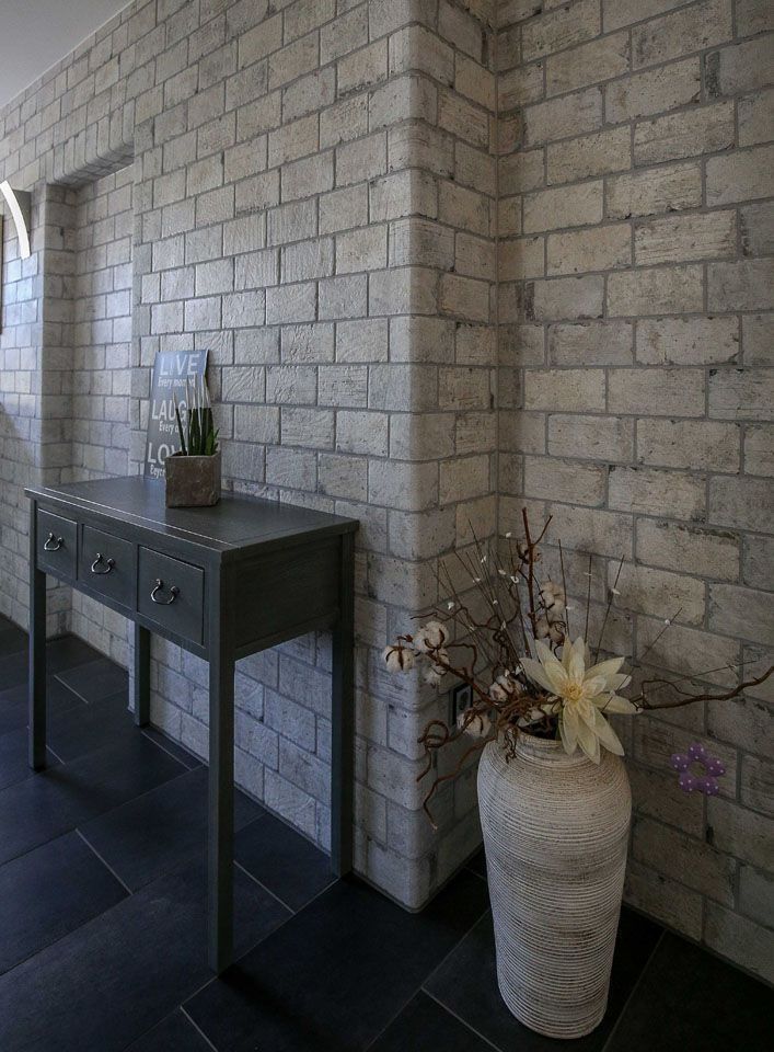 Grauer Backstein-Innenraum mit dunklem Konsolentisch, Vase mit Blumen und dunklem Fliesenboden.