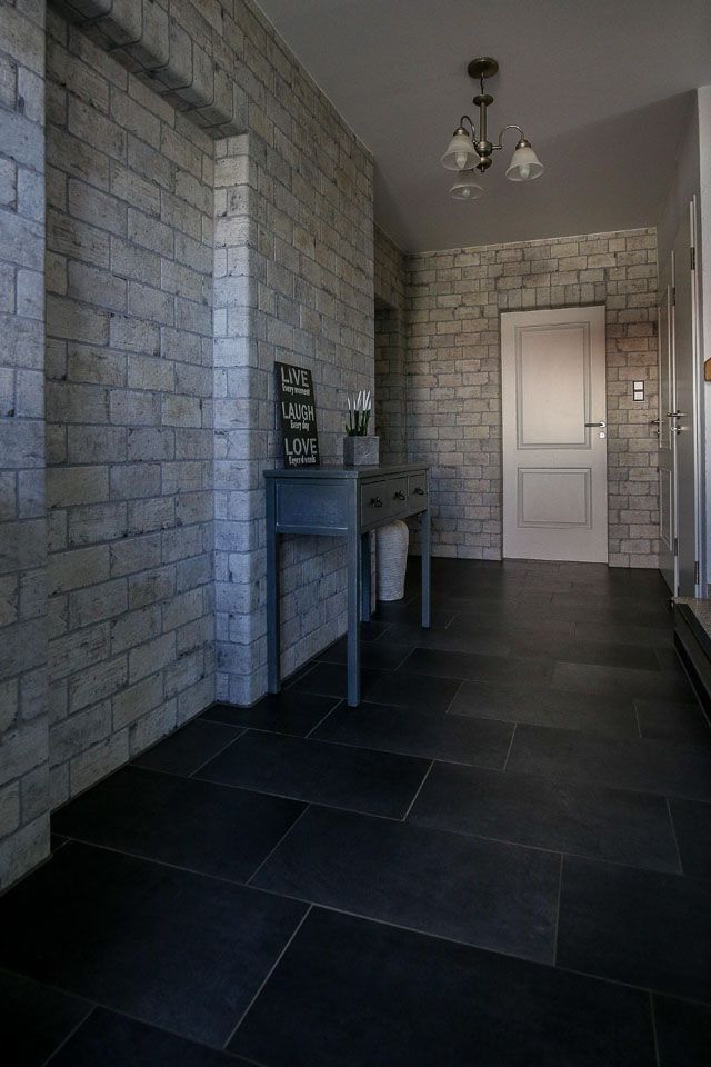 Schmaler Flur mit grauen, ziegelmusterartigen Wänden, dunklem Fliesenboden und einem kleinen Tisch.