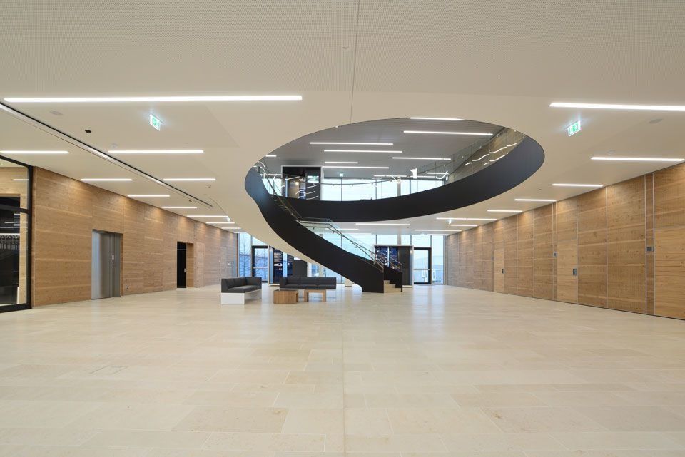 Modernes Interieur mit Wendeltreppe, hellen Wänden und Böden sowie langen rechteckigen Deckenleuchten.