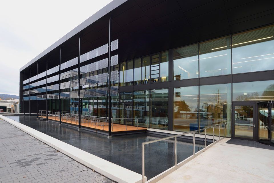 Modernes Gebäude mit Glaswänden, Spiegelbecken und schwarzem Vordach.